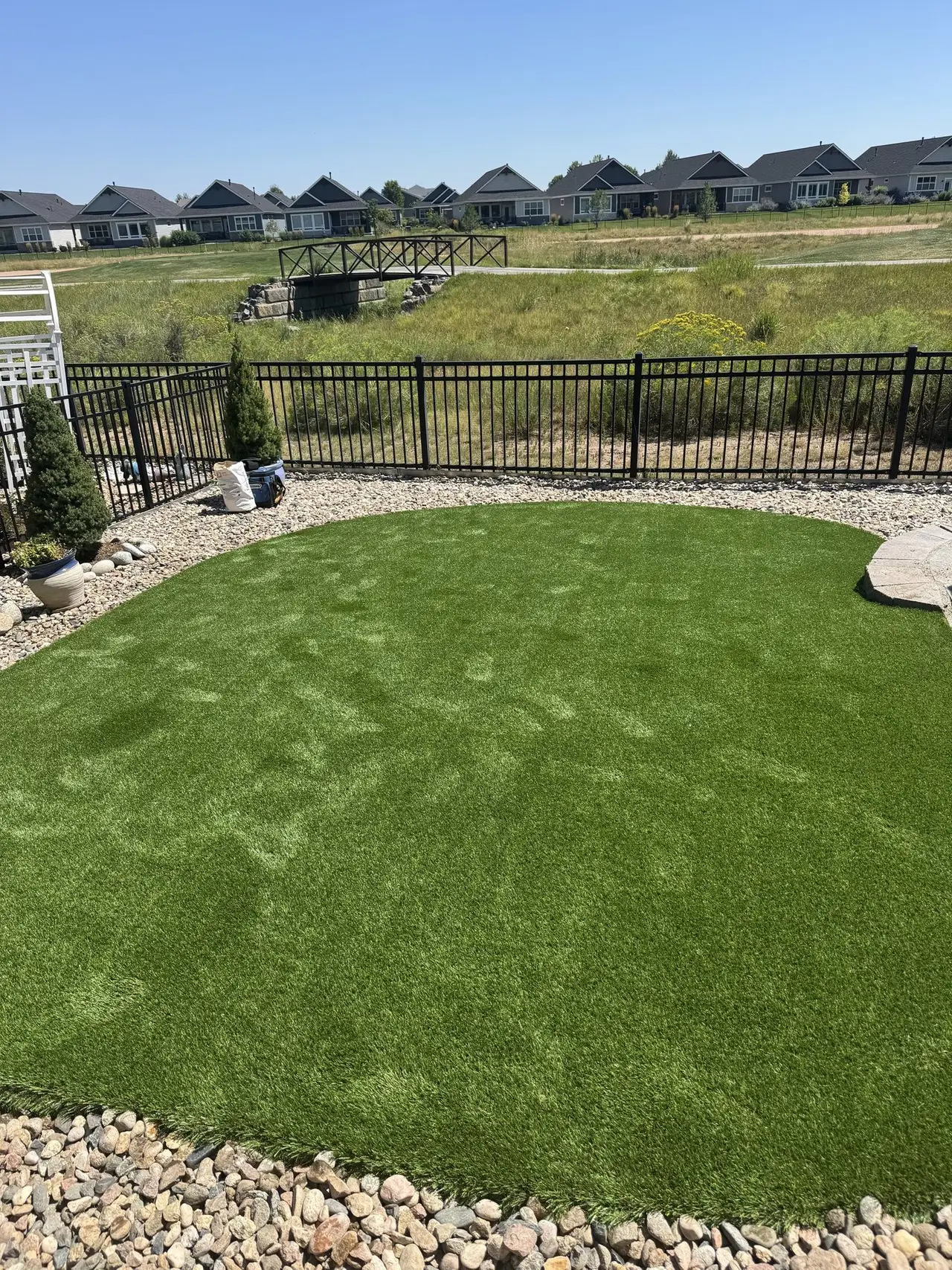 A fenced artificial lawn with a rock border along the fence line