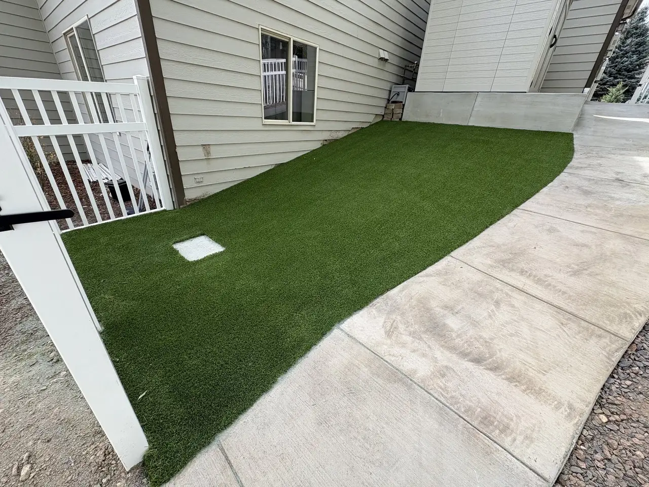 Artificial turf running down a side yard, meeting the concrete path along its edge