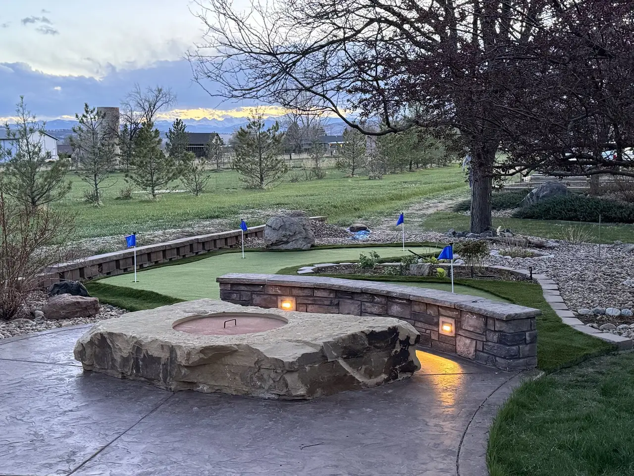 A putting green beside a stone fire pit and seat wall, mountains on the horizon