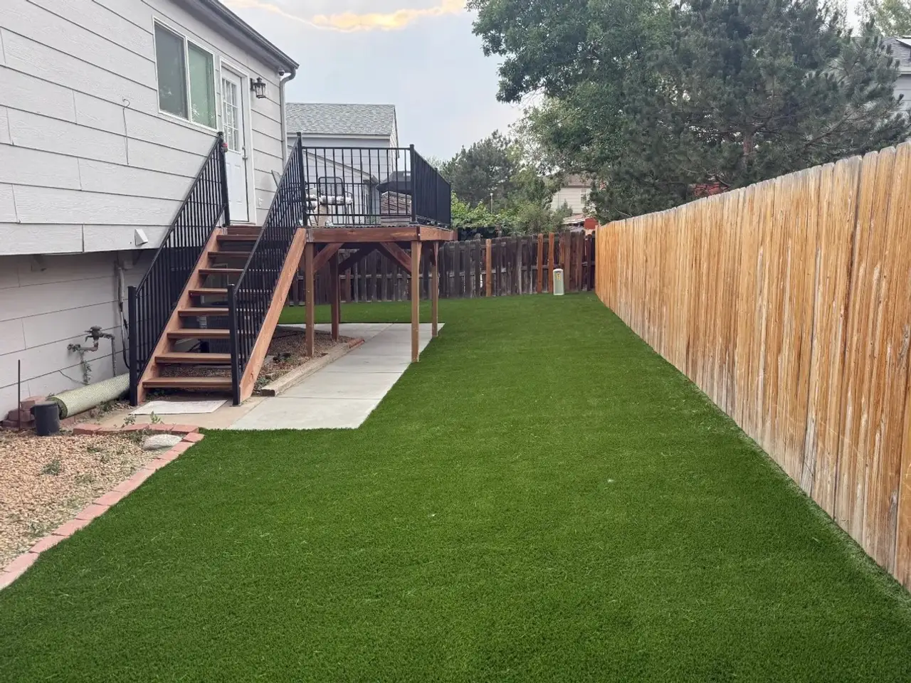 The same side yard covered in artificial turf from the fence to the concrete path, the gravel bed and brick edging kept
